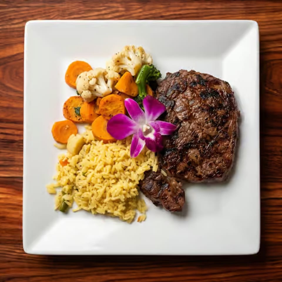 Grilled steak, yellow rice, roasted vegetables, and a purple orchid on a white plate.