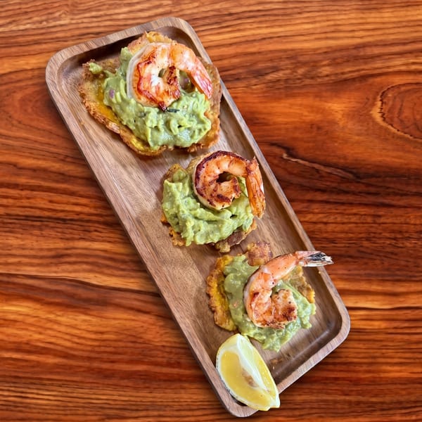 Three shrimp and guacamole tostones with a lemon wedge on a wooden serving tray.